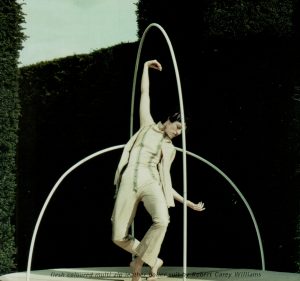 Litza Bixler posed with one arm stretched overhead in all-white costume. Two hoops intertwine above her head.