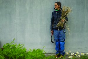 image of artist Amy Franceschini holding wheat and a harvesting tool