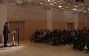 Juan de Marcos stands at a podium addressing a crowded room
