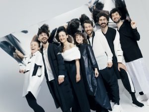 photo of the ensemble standing before a sheet of reflective material and laughing