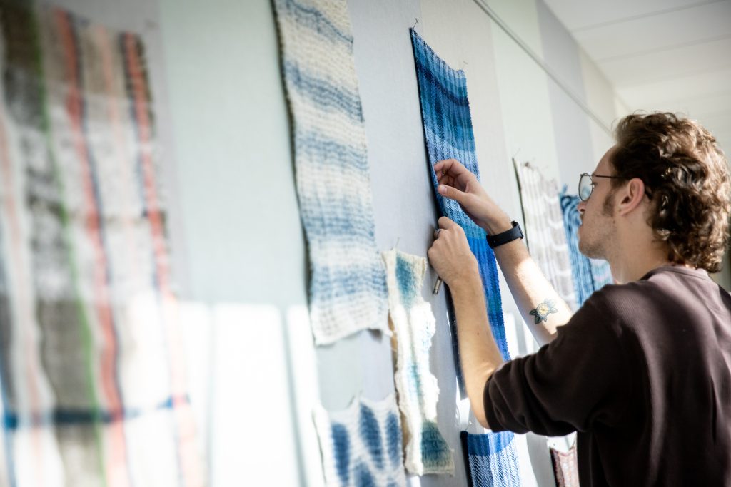 Matthew Lyga examines the weaving technique of a fellow student’s water cloth curing a critique session in associate professor Marianne Fairbanks’ weaving class. (Photo by Catherine Reiland/UW-Madison)