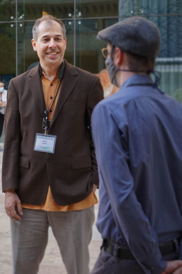 Two men stand facing each other smiling.