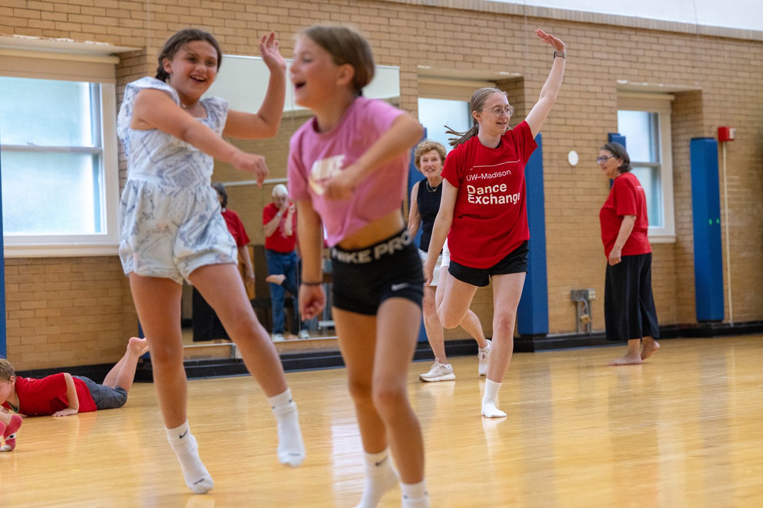 A UW student in a red shirt and two children are all posed mid-dance as two older adults look on.