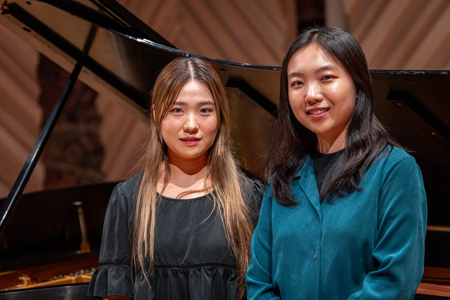 Two students dressed in deep green stand in front of a grand piano.