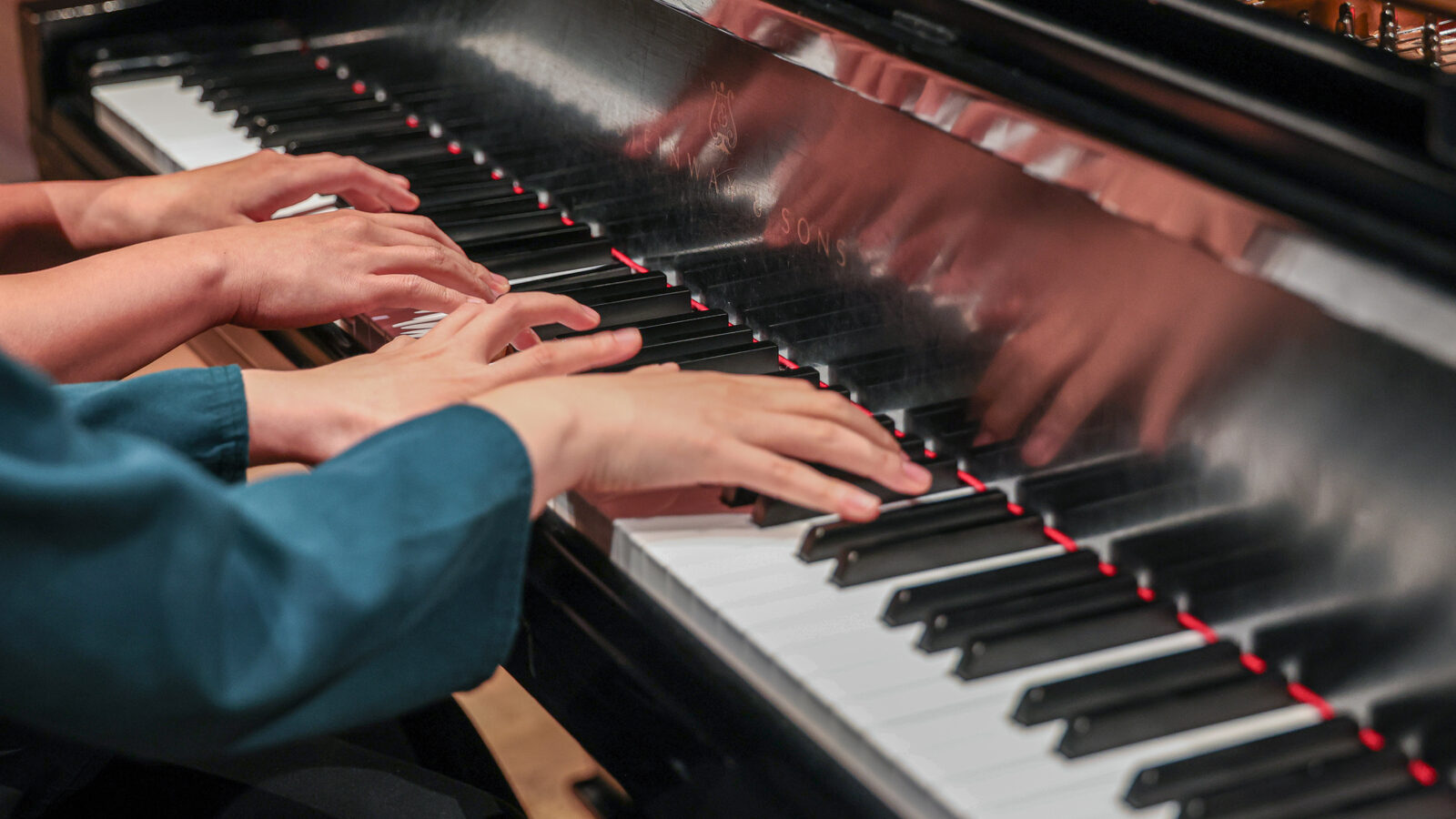 A close up of the two sets of hands at the piano of two students side by side.