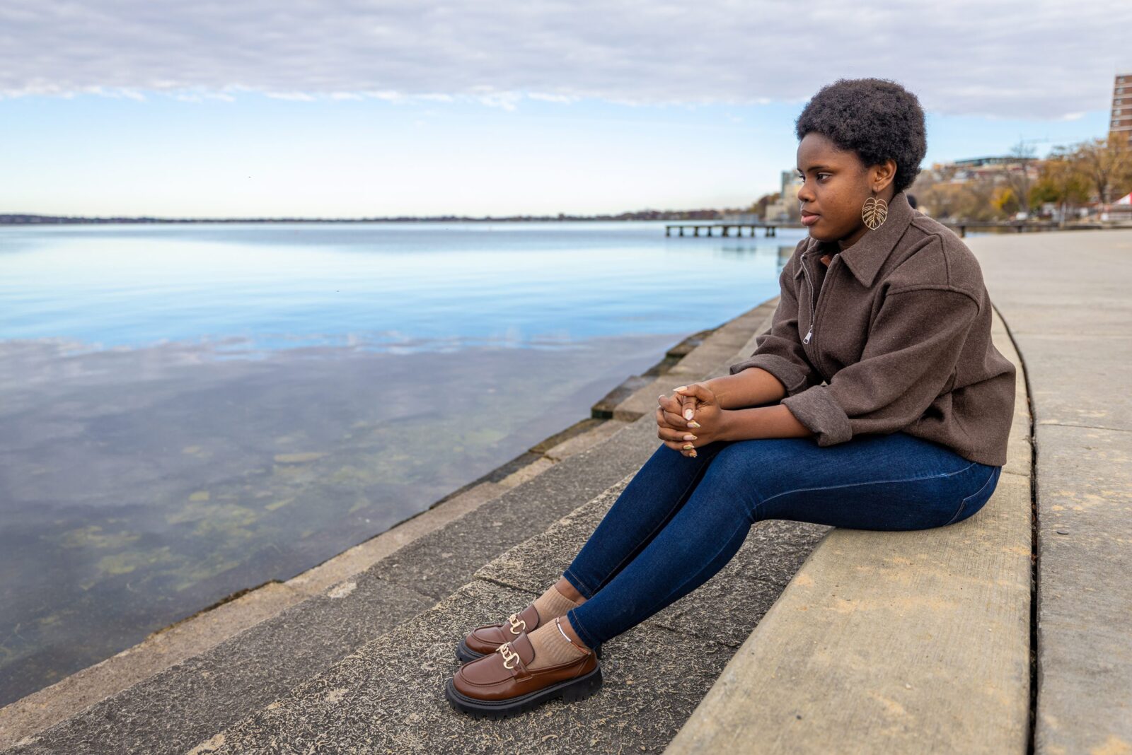 A woman sits on the stone steps looking out over a clear lake.