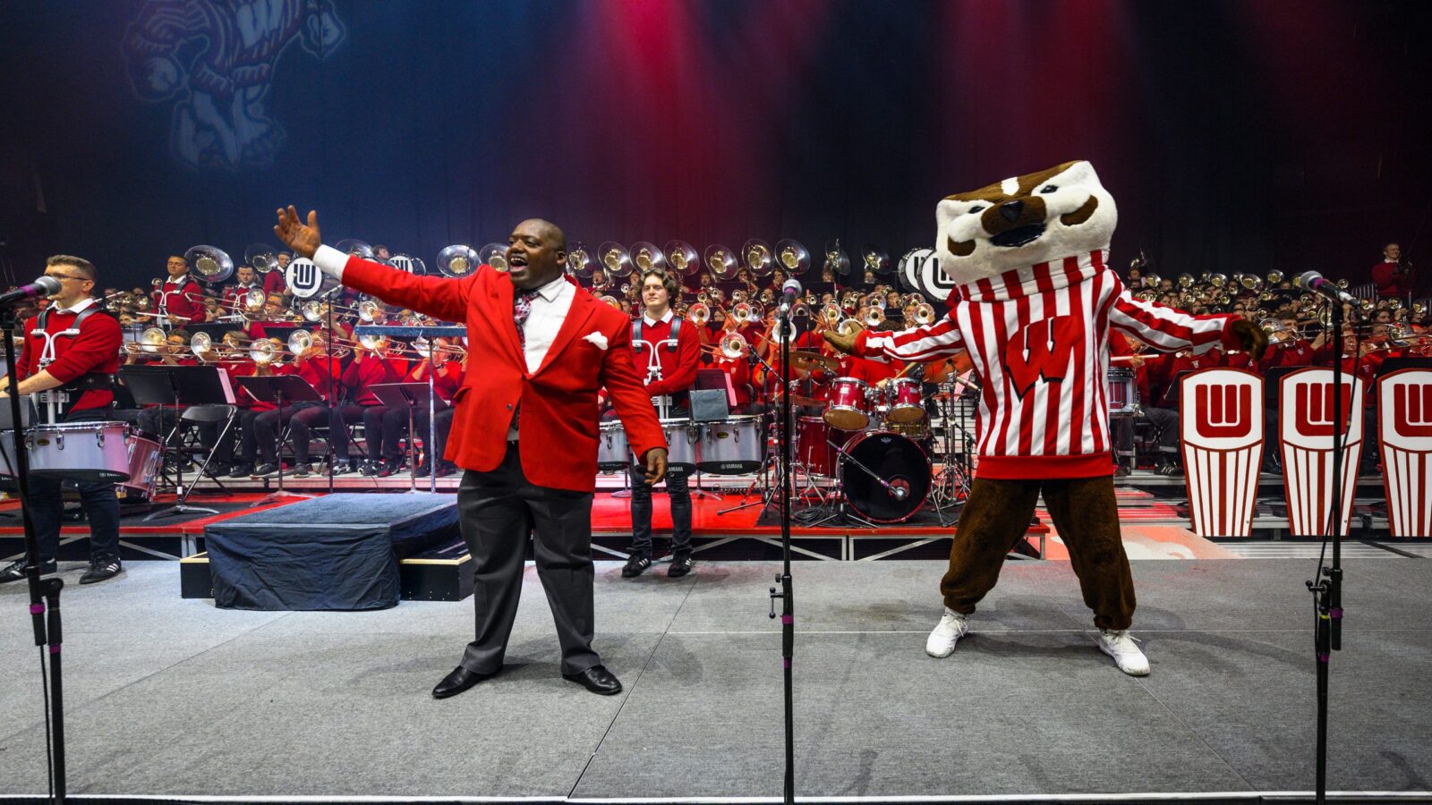 Corey Pompey and Bucky Badger stand with arms raised in front of Varsity Band members.
