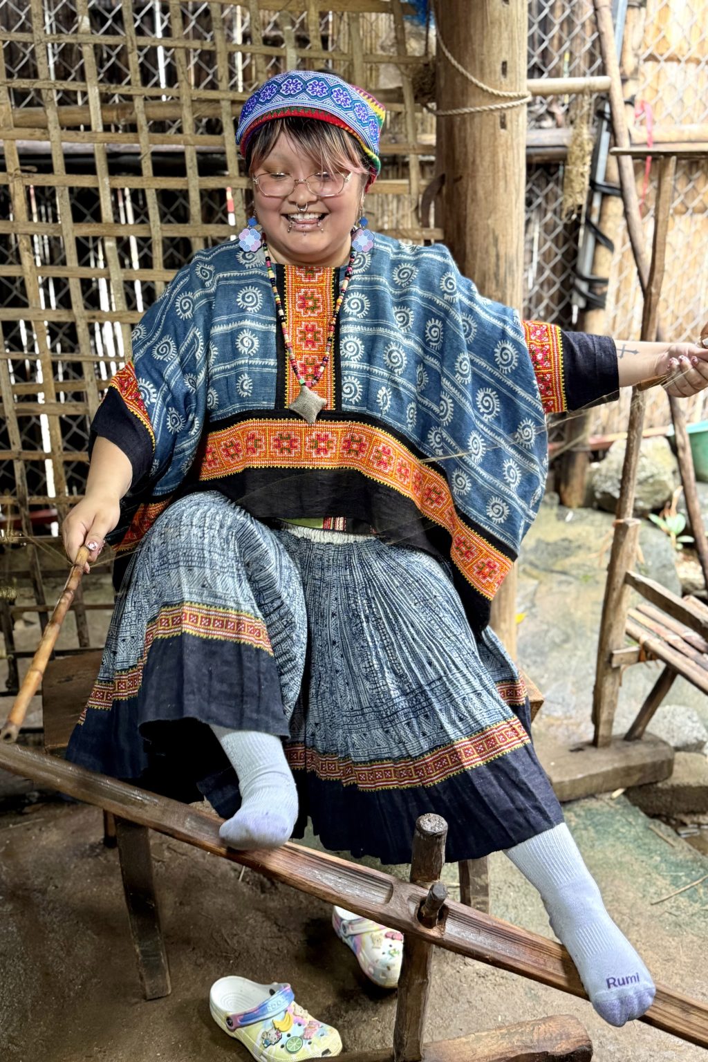 A student is sitting at a loom with her shoes off and her socks on the wooden portion, pedaling with her feet