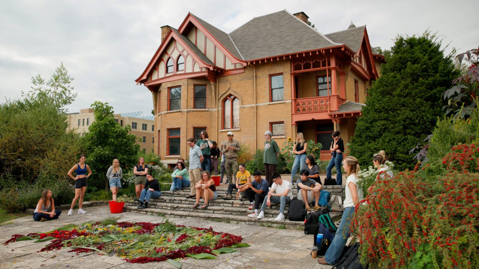 A dozen or more students sit and stand in front of a house at Allen Centennial Garden with a pile of cut flowers in front of them.