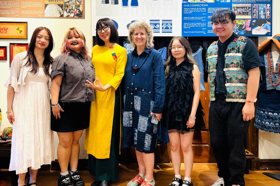 Four students and two mentors stand in front of a colorful exhibition of textiles and fashion collections.