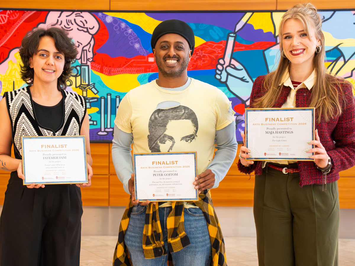 three people holding award certificates pose together in front of a colorful mural