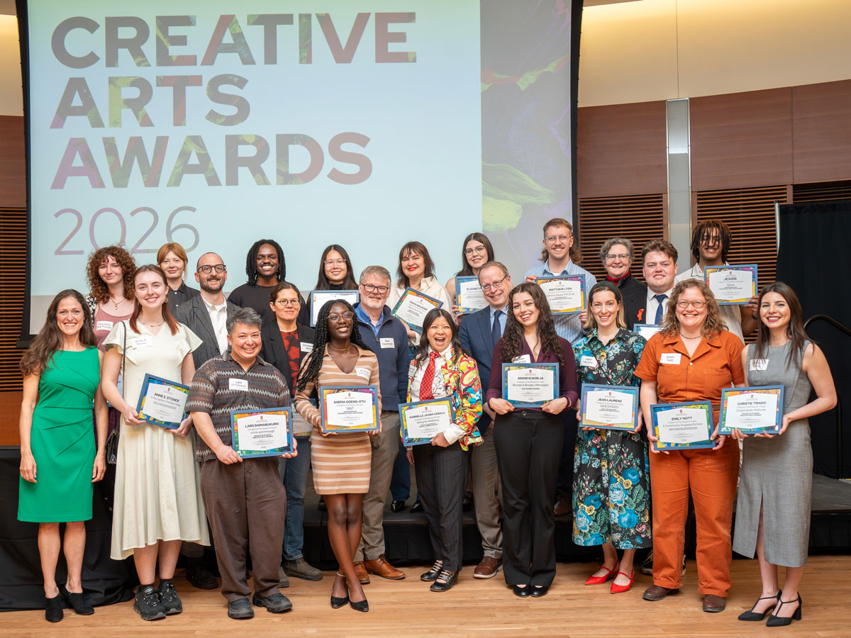 23 people, many holding award certificates, pose together with a large screen that says Creative Arts Awards 2026