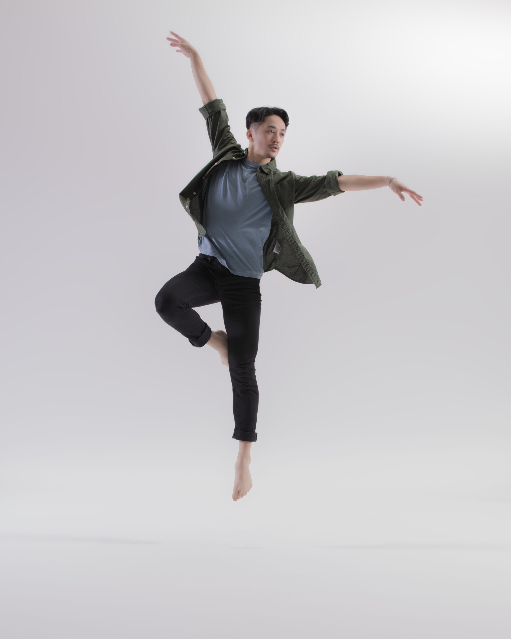 A barefoot dancer wearing regular casual clothing leaps against a white background