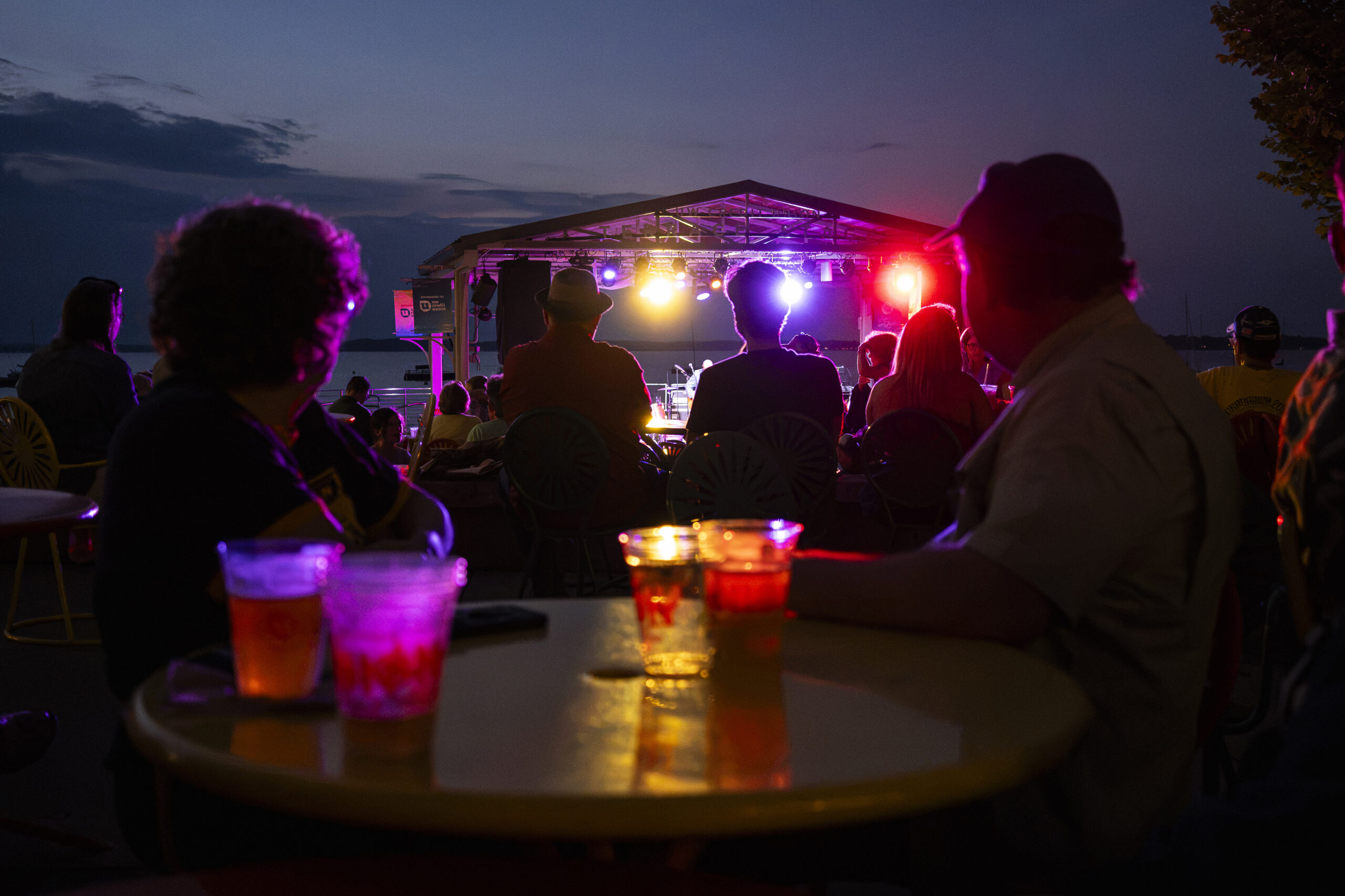 Stage lights shine as people listen to a live music performance at the Memorial Union Terrace at the University of Wisconsin–Madison, and dusk falls to nighttime during summer on Aug. 1, 2026. (Photo by Jeff Miller / UW–Madison)