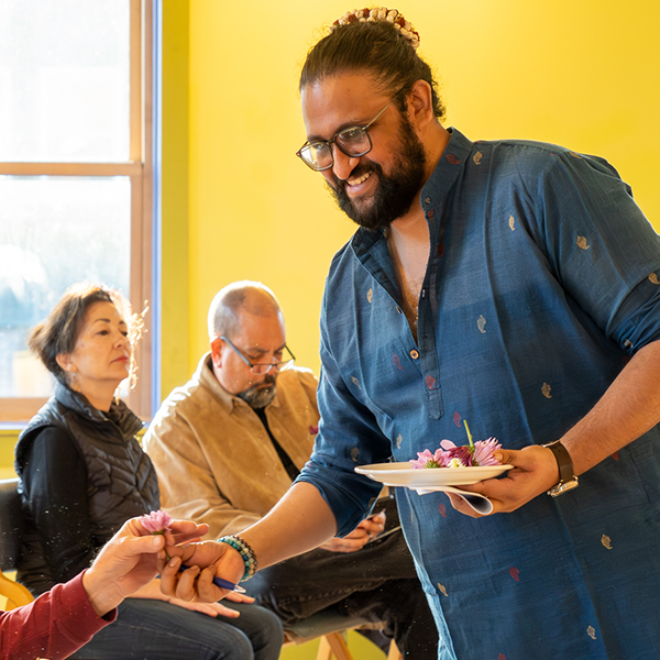artist in residence, handing out flowers to a seated audience in a bright yellow room