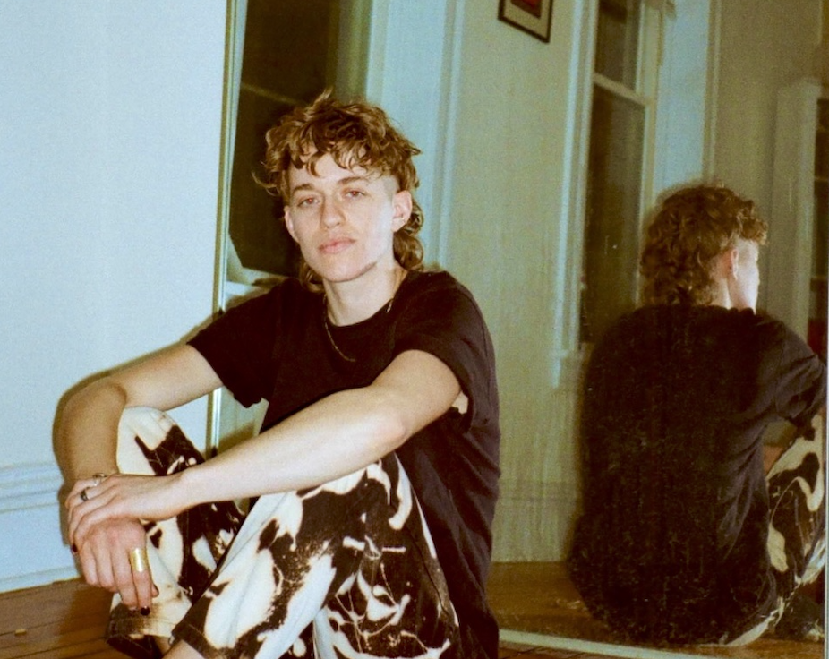 a young person sits on the floor with their back to a mirror, reflecting their back